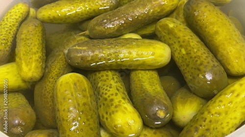 Fresh market pickles in container, closeup of clear plastic tub packed with brined cucumbers, glistening brine