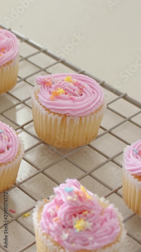 Vertical video: Panning lens centering cupcake on counter, pink rosette pastel stars on rack