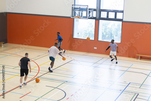 Obraz na plátně Diverse male friends playing basketball on gym court dribbling three balls near