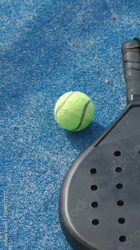 Vertical video: Rolling neon tennis ball nudging from camera move on blue court beside black paddle