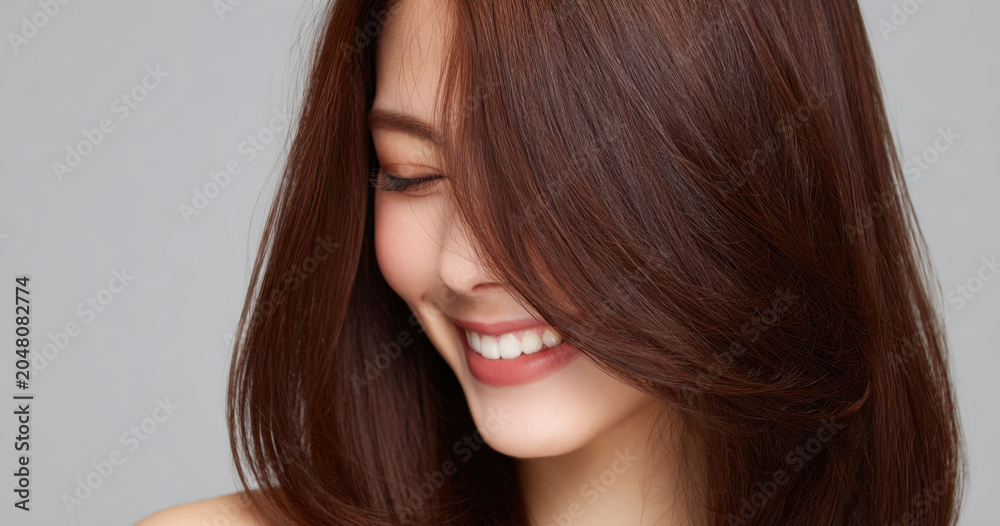 Naklejka premium Smiling woman with smooth chocolate brown hair, close up portrait on gray background