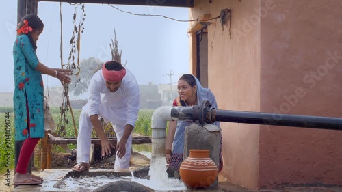 Village couple and their daughter enjoying together on a beautiful summer day. Happy Indian farmer and his small family playing with freshwater near a tubewell - village lifestyle concept