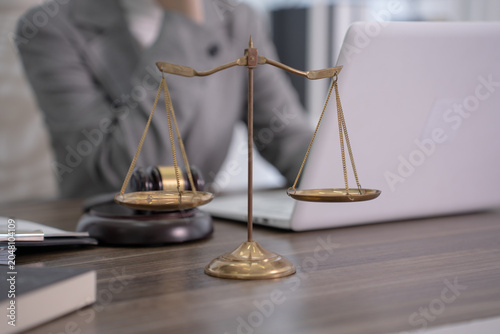 A pair of vintage golden scales of justice stands prominently on a wooden desk next to a blurred gavel and a modern laptop in a professional legal office setting.