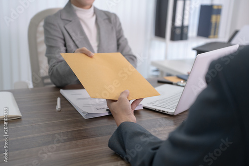 A professional lawyer extends a yellow legal envelope to her client while sitting in her office for a consultation.