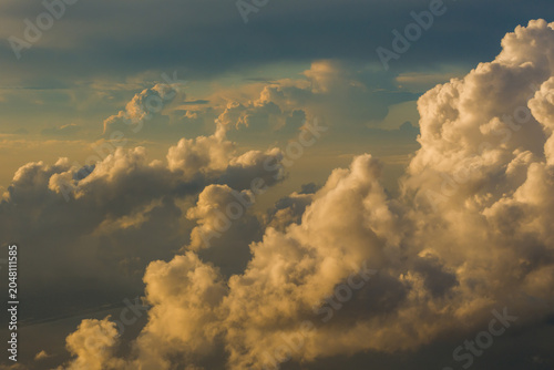 Принти на полотні Dense massive cumulus thunderhead clouds illuminated by intense golden sunlight creating deep shadows in the evening sky