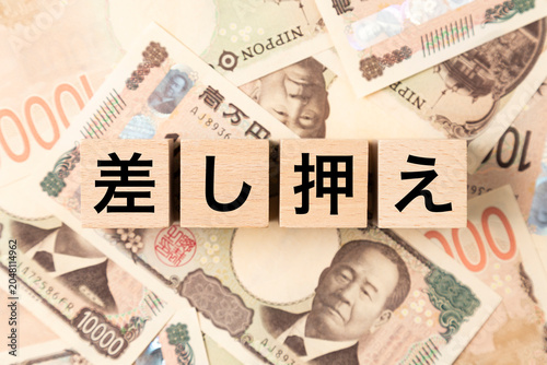 「差し押え」と書かれたブロックとたくさんの一万円札