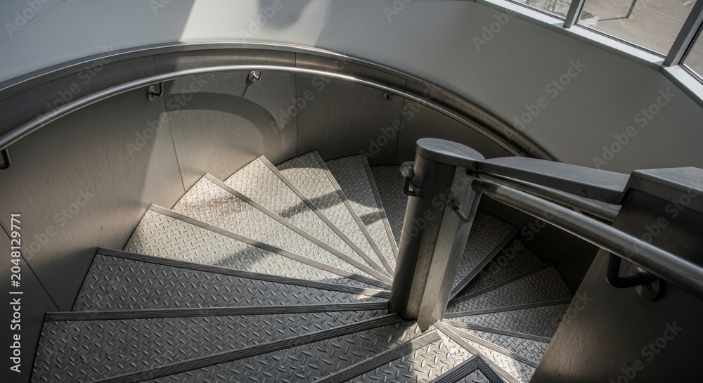Fototapeta premium Modern Spiral Staircase with Natural Light and Shadow Play.