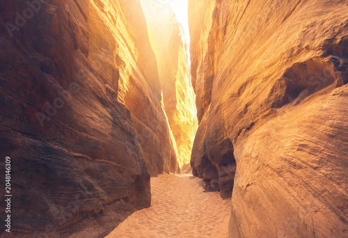 Foto A narrow desert slot canyon with towering orange sandstone walls and a sandy pat