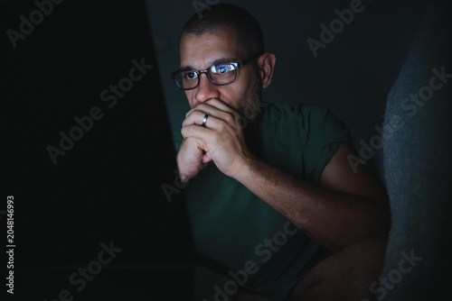 Man with glasses focusing on his laptop screen at night