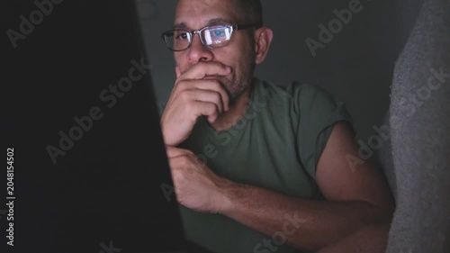 Serious man with glasses feeling tired and overworked while using a computer in a dark room