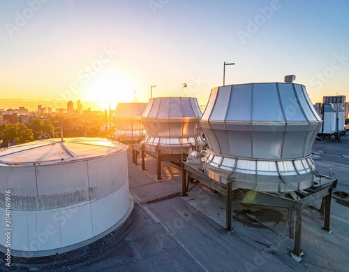An industrial truck travels past large metal grain silos and storage tanks on a rural road at sunset
