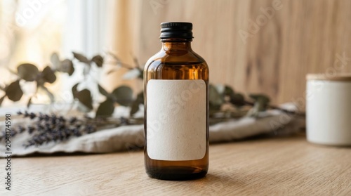 A dark amber glass bottle with a black metal cap sits on a wooden table. A blank white label is affixed to the bottle.