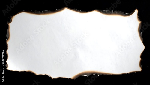 A white rectangular paper sheet with charred edges, set against a stark black background