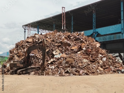 Industrial metal recycling facility with a mountain of old rusty waste materials and sorting equipment.