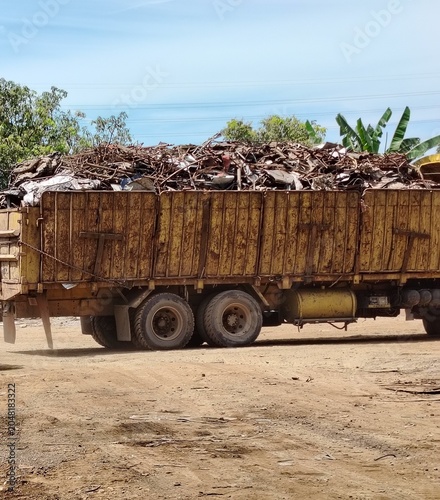 Heavy duty freight truck carrying a massive load of discarded metal waste along a dusty industrial yard road.