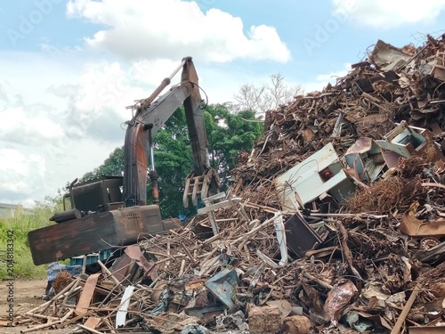 Tracked excavator operator working beside a gigantic pile of scrap metal for sustainable material recovery.