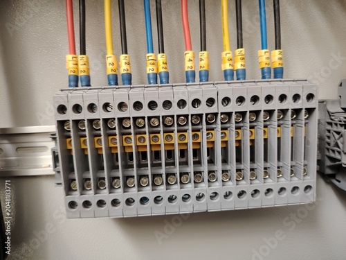 Electrical connection terminal strip inside a distribution control panel box with yellow cable marker tags.
