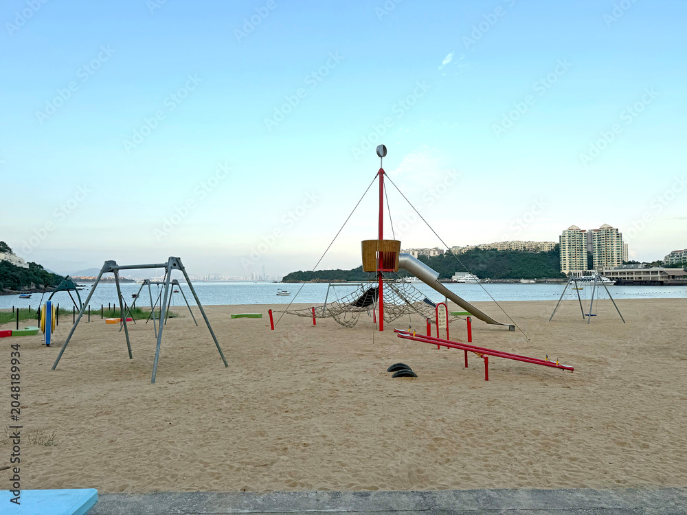Fototapeta premium Beach playground with swings and slides overlooking the ocean and city skyline