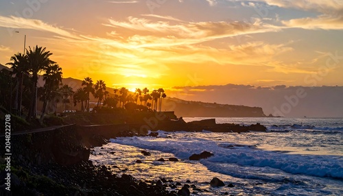 A vibrant sunset casts golden light over a coastal landscape. Silhouetted palm trees line a shoreline as waves crash