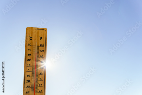 Thermometer showing rising mercury against a bright sun and clear blue sky, illustrating concept of heatwave and climate change
