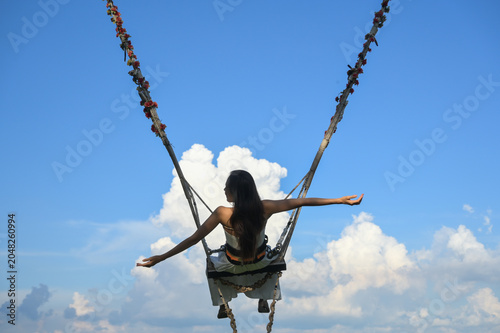 Fotografía A person swings high in the air against a bright blue sky with fluffy white clouds, enjoying a sense of freedom and exhilaration
