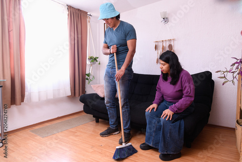 Quadro su tela Man Sweeping Floor While Woman Sits on Sofa