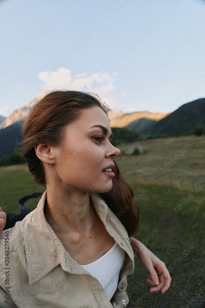 Naklejka premium Cheerful woman outdoors, smiling softly, sunlit moment, relaxed posture, casual attire, natural colors, open landscape background