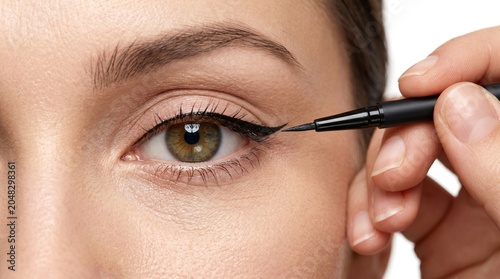Macro shot of makeup artist hand applying black liquid eyeliner with a precise brush on a woman green eye