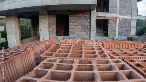Bild auf Leinwand Close-up of hollow red clay bricks in the foreground of a building construction site with a concrete and briquette structure in progress