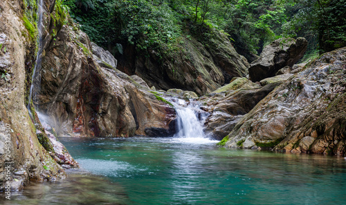 Sanzhanxi river in Taroko National Park. Scenic small waterfall flows into clear blue pool. Lush green forest surrounds rocky cliffs in Hualien, Taiwan.