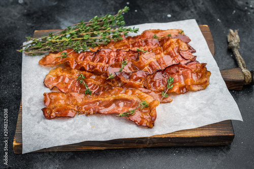 фотографія Smoked streaky bacon cooked to sizzling crispness with shiny pork surface resting on parchment and herbs great for culinary designs