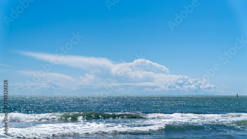 Wide sea horizon with blue water and white breaking waves under a clear sky with a large white cloud. Minimalist coastal landscape in Dalaman, Turkey.