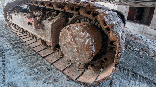 Close-up of heavy machinery rusty metal tracks and drive sprocket on a muddy construction site. Concept of industrial power, earthmoving, and heavy equipment.