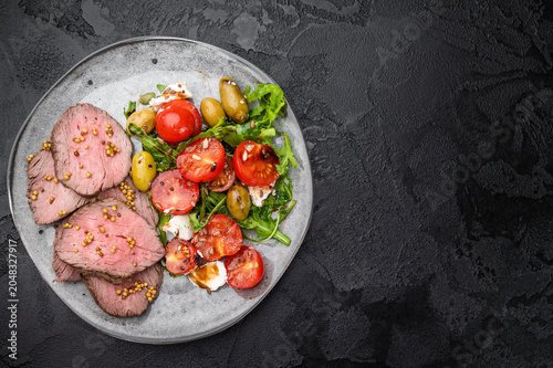 Roast beef salad with medium rare beef slices arugula tomatoes olives and cheese on dark stone background top view copy space