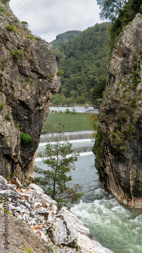Namnam River cascade over a stepped weir between moss covered rocky cliffs and dense pine forest in Mugla, Turkey. Vertical photo