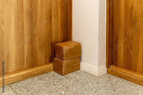 Two small cardboard parcels stacked in a hallway corner between wooden doors. Useful for delivery, shipping, online order, moving, package, storage and home interior concepts.