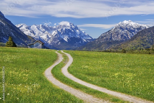 Mountain path through spring meadow with hay barn in front of Zugspitzgruppe 2962m in the Wetterstein Mountains and Kramer 1922m, Eschenlohe, Loisachtal, Das Blaue Land, Upper Bavaria, Bavaria, Germany