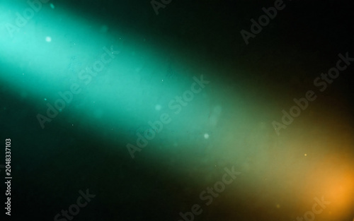 Abstract light beams shine in green and orange on dark background