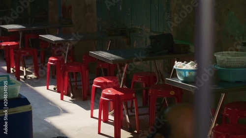 Empty street asian food restaurant patio with red stools and tables in a sunlit alley in Bangkok, Thailand during daytime