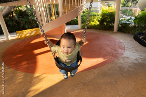 Happy toddler boy swinging in outdoor playground