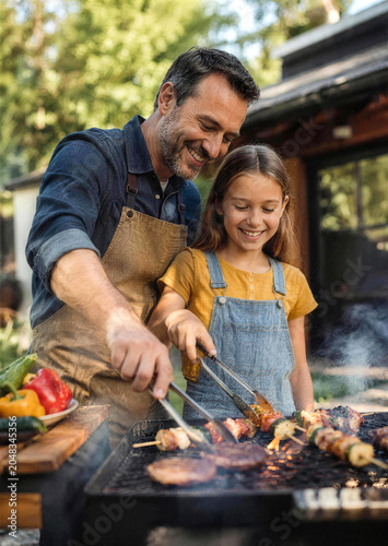Happy father and daughter grilling meat on backyard barbecue with daughter grilling barbecue
