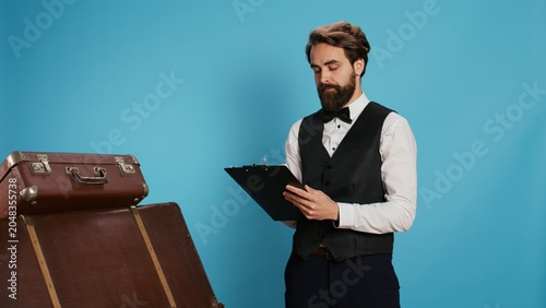 Tableau sur toile Doorman verifying checklist of guests, holding register log on clipboard to check hotel visitors in studio