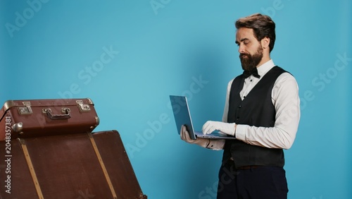 Cuadro en lienzo Hotel staff reviews list of guests on online bookings while using laptop and standing next to stack of suitcases