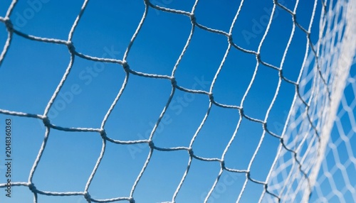 High-contrast abstract sports photography showing a white soccer goal net tightly stretched against a vivid clear blue sky, capturing the essence of team sports and winning performance.