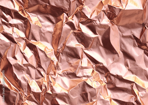 Close-up of crumpled, metallic surface. The rose gold material has reflective qualities and texture with sharp angles and varying shades