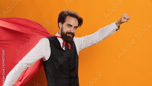 Obraz na plátně Elegant butler with red cape posing on camera while he acts like superhuman at luxury restaurant, yellow studio