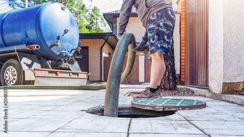 Septic tank service takes place outside a residential home with a sewage truck present on a sunny day