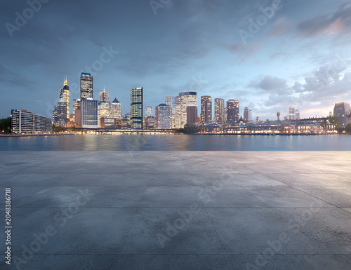 A scenic urban landscape showcases a concrete foreground leading to a sparkling cityscape along a serene body of water. Twilight hues dominate