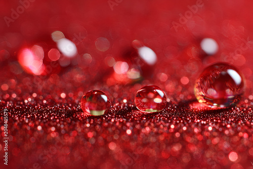 Close-up macro of water droplets resting on a shimmering, textured red surface, creating a bokeh effect