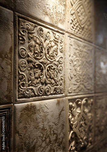 Close-up of intricately designed, cream-colored, textured tiles with embossed patterns and depth, mounted on a wall